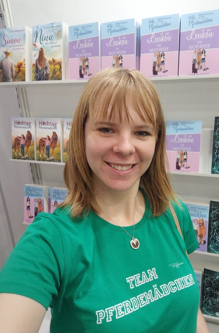 Carina Warnstädt Autorin Carina Warnstädt vor einem Regal mit Pferdebüchern. T-Shirt Aufschrift: Team Pferdemädchen.